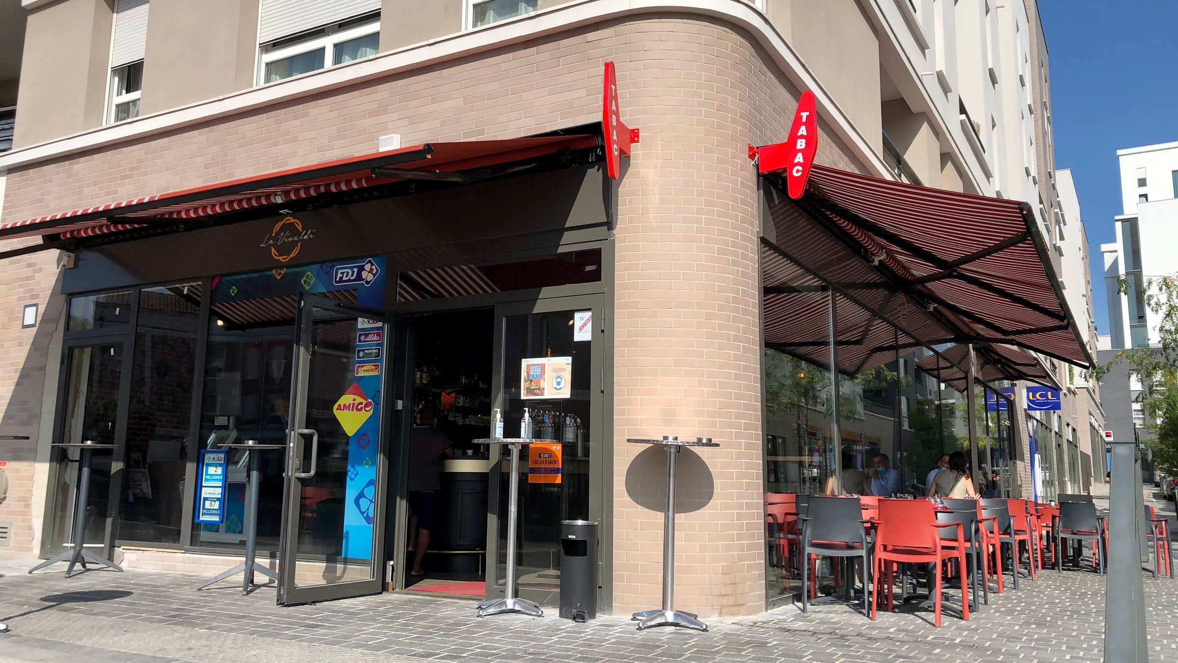 L'angle du Vivaldi, façade en brique claire, stores rouges et terrasse sur l'avenue de la Gare